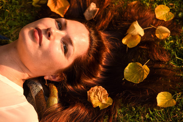 Yerde yatan olgun bir kadının portresi, sonbahar yaprakları saçlarına dağınık. - Fotoğraf, Görsel
