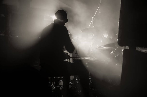 Egy dobos sziluettje, aki dobfelszerelést játszik a színpadon a reflektorfények fénysugaraiban. Rock koncert. - Fotó, kép