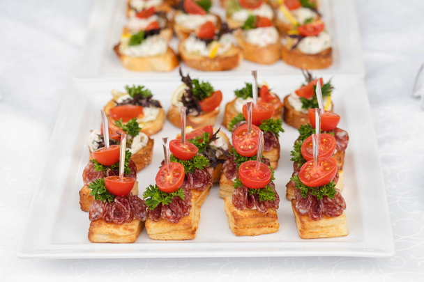 Delicious canape with sausage and tomato.Canapes on white ceramic plates at wedding reception. - Foto, Imagen
