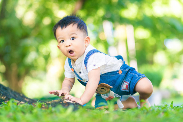 Vicces kisfiú mászik a zöld füvön rét a városi parkban - Fotó, kép