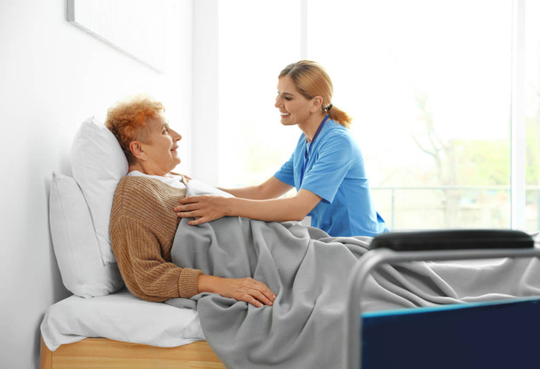 Pielęgniarka w mundurze wspomagającym starszą kobietę w pomieszczeniu - Zdjęcie, obraz