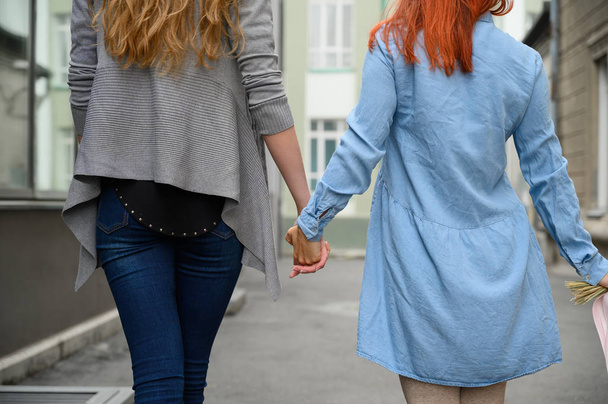 Vztahy stejného pohlaví. Šťastný lesbický pár kráčí po ulici a drží se za ruce. Záda dvou krásných žen na rande s kyticí sušených květin. Lgbt. - Fotografie, Obrázek