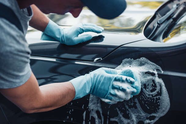 partial view of car cleaner washing car with sponge and detergent - 写真・画像