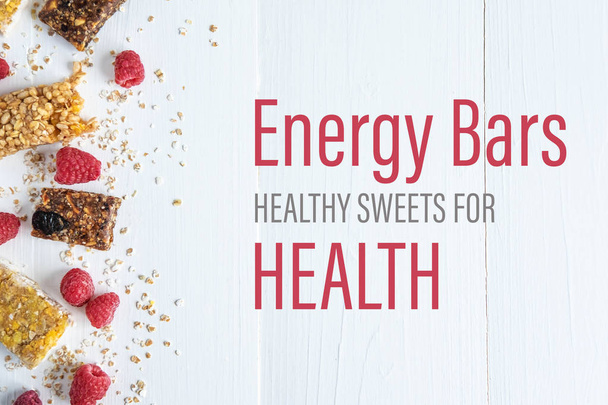 Energia szeletek egészséges édességek az egészségre. A felirat egy fehér fa háttér granola és friss málna. Egészséges gabonapehely-reggeli - Fotó, kép