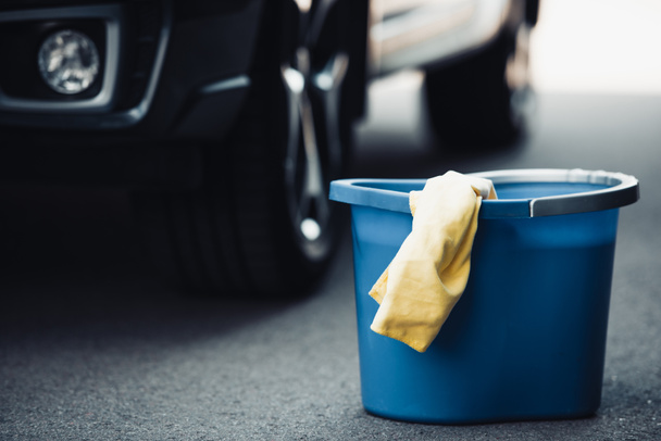 blue bucket and yellow rag on asphalt near black car - Фото, изображение