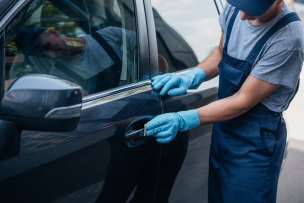 Kırpılmış araba temizleyicisi kapı kolunu paçavrayla siliyor. - Fotoğraf, Görsel