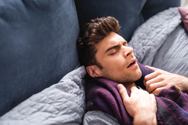 sick and handsome man in scarf with closed eyes lying in bed  - Fotoğraf, Görsel