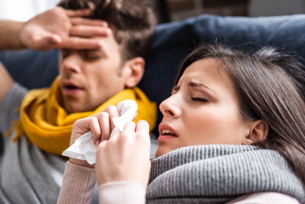 selective focus of sick girlfriend sneezing and holding napkin in apartment  - Valokuva, kuva