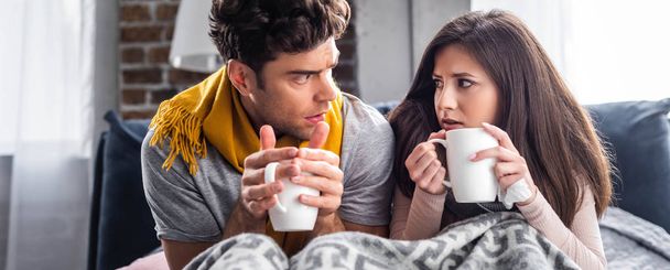panoramic shot of sick girlfriend and boyfriend holding cups with tea  - Fotó, kép