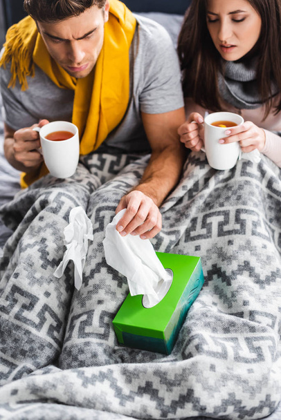 high angle view of sick girlfriend holding cup and boyfriend taking napkin  - Photo, Image