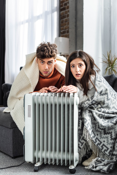 attractive girlfriend and boyfriend covered with blankest warming up near heater  - 写真・画像