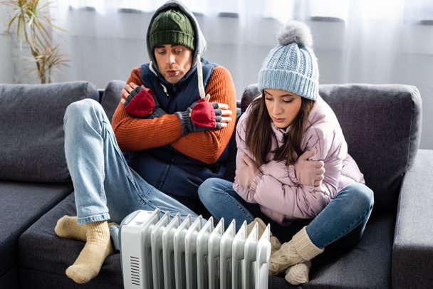 attractive girlfriend and boyfriend in winter outfit warming up near heater  - Photo, Image