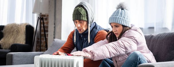 panoramic shot of girlfriend and boyfriend in winter outfit warming up near heater  - Photo, Image