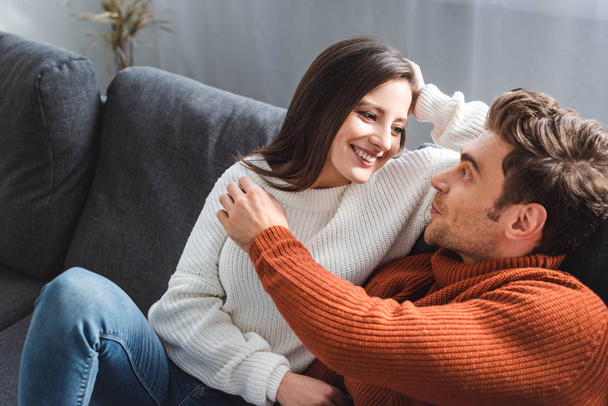 attractive girlfriend in sweater and handsome boyfriend hugging and sitting on sofa  - Foto, Imagem