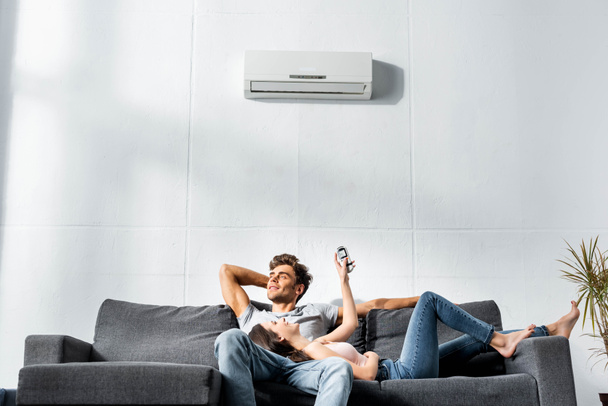 attractive girlfriend switching on air conditioner and lying on legs of handsome boyfriend  - Photo, Image