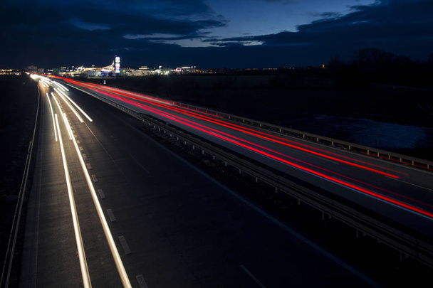 Pohyb rozmazané světelné stopy zářící do tmy dálniční dopravy do města těsně po západu slunce. - Fotografie, Obrázek
