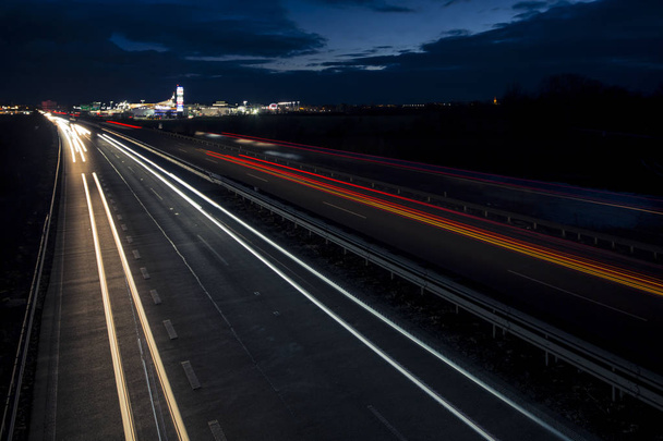 Motion blurred light tracks glowing to the darkness of highway traffic to the city just after sunset. - Valokuva, kuva