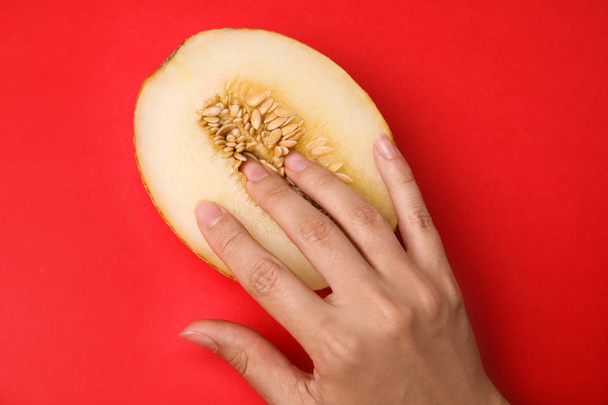Young woman touching half of melon on red background, top view. Sex concept - Foto, imagen