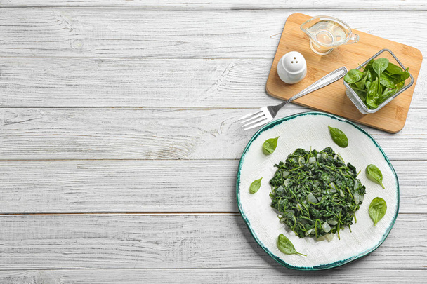 Flat lay composition with tasty cooked spinach and space for text on white wooden table. Healthy food - Zdjęcie, obraz