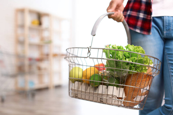 Man with shopping basket full of products in grocery store, closeup - Photo, image