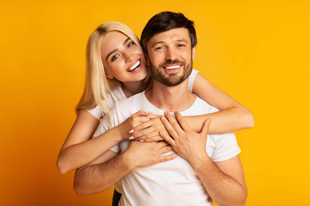 Happy Couple Hugging Standing Over Yellow Background, Studio Shot - Foto, imagen