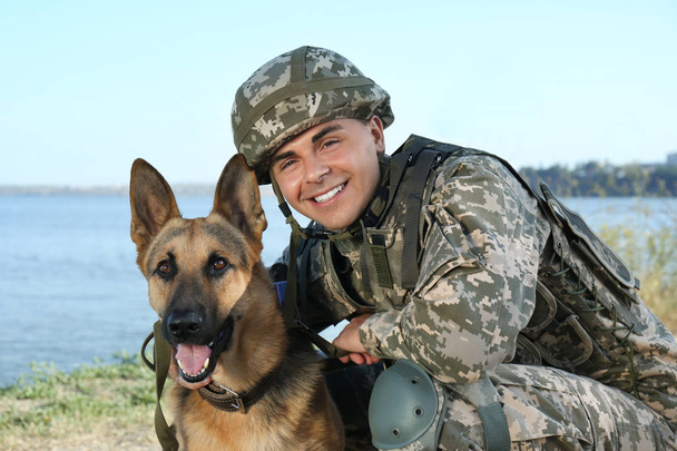 Man in military uniform with German shepherd dog near river - Фото, зображення