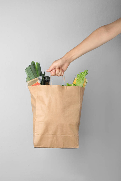 Woman holding paper bag with fresh vegetables on grey background, closeup - Фото, зображення