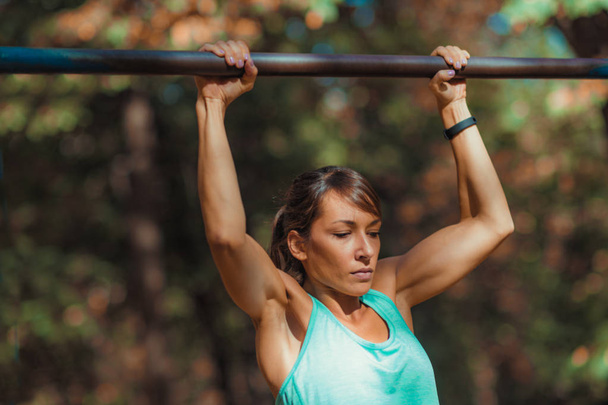 Woman doing pull-ups in the park   - Photo, image