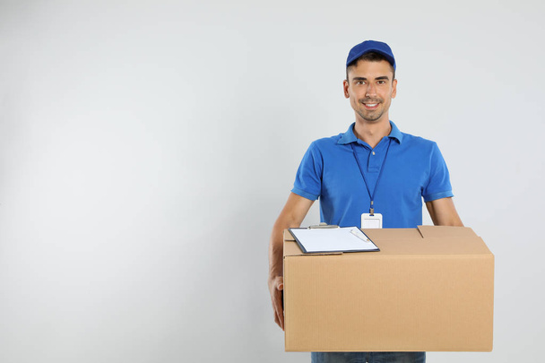Happy young courier with cardboard box and clipboard on white background. Space for text - Foto, Bild