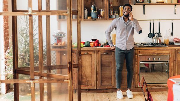 Giovane uomo nero che parla sul cellulare in cucina
 - Foto, immagini
