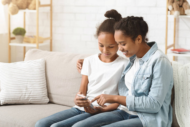Two adorable sisters using smartphone on sofa at home - Foto, imagen