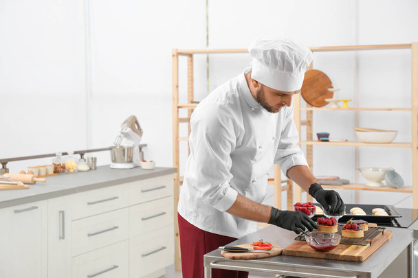 Male pastry chef preparing desserts at table in kitchen. Space for text - Foto, afbeelding