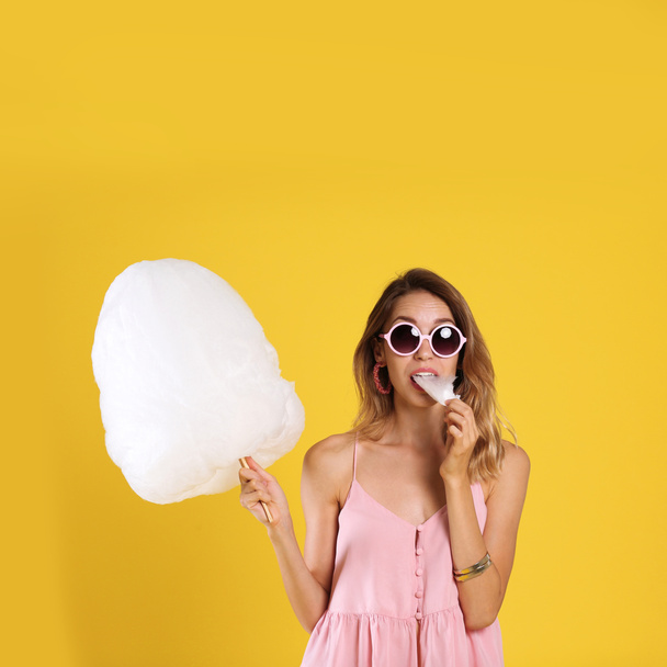 Happy young woman eating cotton candy on yellow background - Foto, afbeelding