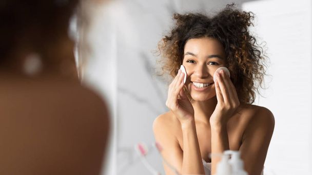 Афроамериканець дівчина тримає ватяні колодки очищення обличчя у ванній кімнаті - Фото, зображення