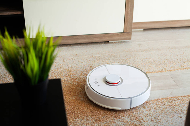 Slim huis. Robot stofzuiger voert automatische reiniging van het appartement op een bepaald moment - Foto, afbeelding