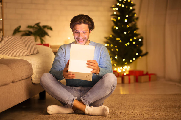 schöner Mann öffnet Geschenkbox gegen Weihnachtsbaum - Foto, Bild