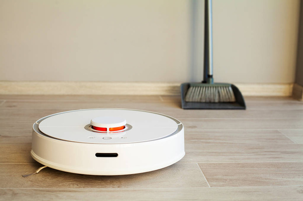 Slim huis. Robot stofzuiger voert automatische reiniging van het appartement op een bepaald moment - Foto, afbeelding
