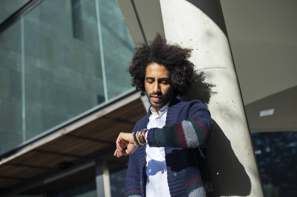 Young handsome man with afro hair Checking the time on wrist watch - 写真・画像