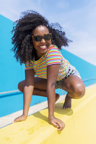 Young african woman with sunglasses crouched while looking to camera - Foto, Imagem