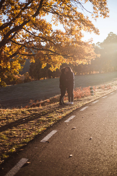 Jeune couple embrassant le long de la route asphaltée dans la forêt colorée de hêtres et chênes d'automne. Route d'automne en montagne. Concept amour et nature
. - Photo, image