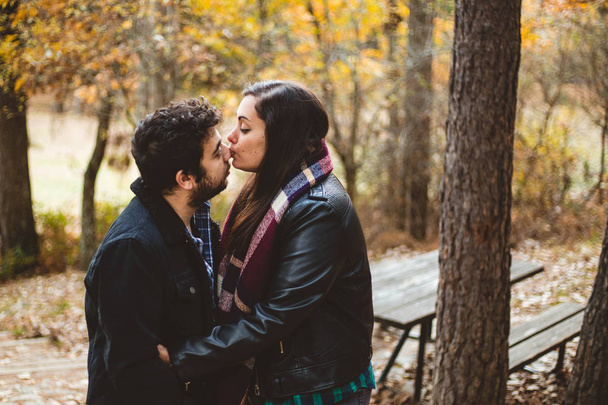 Para zakochanych całuje się jesienią w jesiennym lesie, ciesząc się pięknym dniem. Para całuje się w kolorowym pomarańczowo-żółtym parku. - Zdjęcie, obraz
