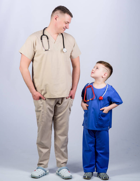 Want to be doctor as dad. Cute kid play doctor game. Family doctor. Pediatrician concept. Medicine and health care. Father doctor with stethoscope and little son physician uniform. Future profession - Foto, afbeelding