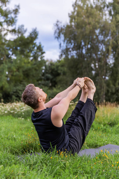 Inspired man doing yoga asanas in city park. Fitness outdoors and life balance concept. Boat Pose or Navasana. - Фото, изображение