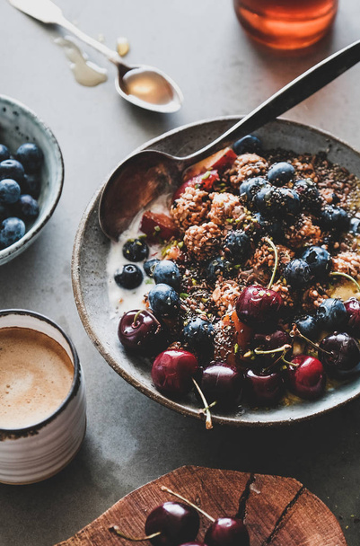Healthy vegan breakfast set. Quinoa oat granola coconut yogurt bowl with fruit, seeds, nuts, berries and cup of coffee over grey concrete background. Clean eating, vegetarian, dieting food concept - Fotó, kép