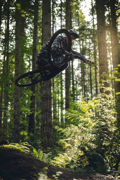 Stijlvolle Mountainbike Air met zijdelingse truc over bosbomen - Foto, afbeelding