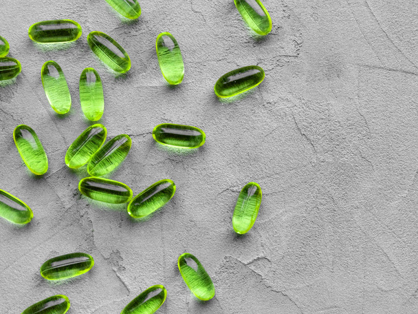 green soft gelatin transparent capsules laid out on a gray concrete background with copy space . The concept of pharmacology, homeopathy and medicine - Foto, Bild