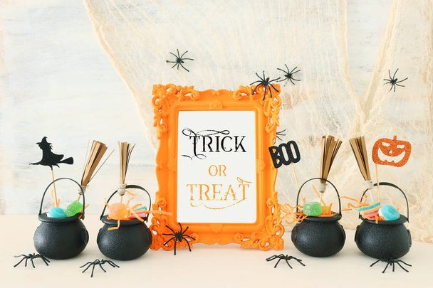 holidays image of Halloween. Witcher cauldron, broom, candies and spiders over white wooden table - Фото, зображення