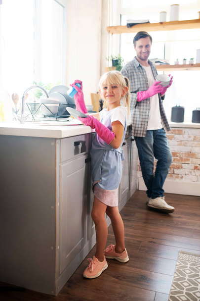 Lovely daughter wearing pink gloves washing the dishes - Fotografie, Obrázek