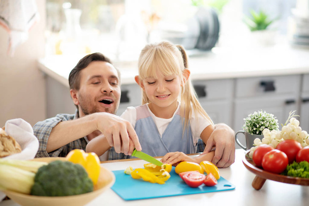 Blonde daughter smiling while cutting peppers with daddy - Foto, Bild