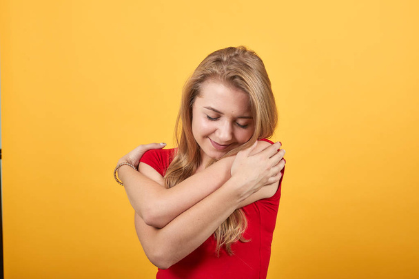 junges blondes Mädchen in rotem T-Shirt über orangefarbenem Hintergrund zeigt Emotionen - Foto, Bild